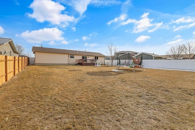 rear view of house featuring a trampoline, a fenced backyard, a yard, and a wooden deck