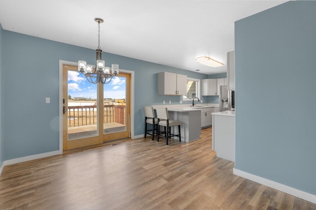 kitchen with light wood finished floors, a chandelier, light countertops, a kitchen breakfast bar, and a sink