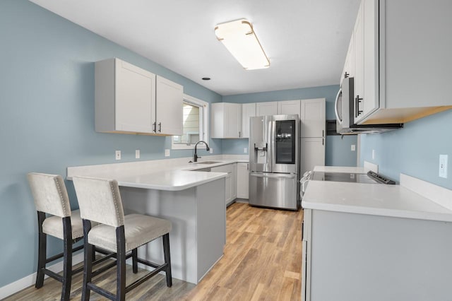 kitchen featuring a breakfast bar, light wood-type flooring, a peninsula, stainless steel appliances, and a sink