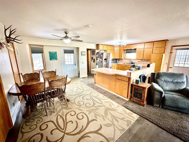 kitchen with a peninsula, light wood-style flooring, a sink, light countertops, and stainless steel refrigerator with ice dispenser