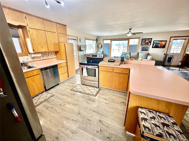 kitchen with light wood finished floors, stainless steel appliances, light countertops, open floor plan, and tasteful backsplash