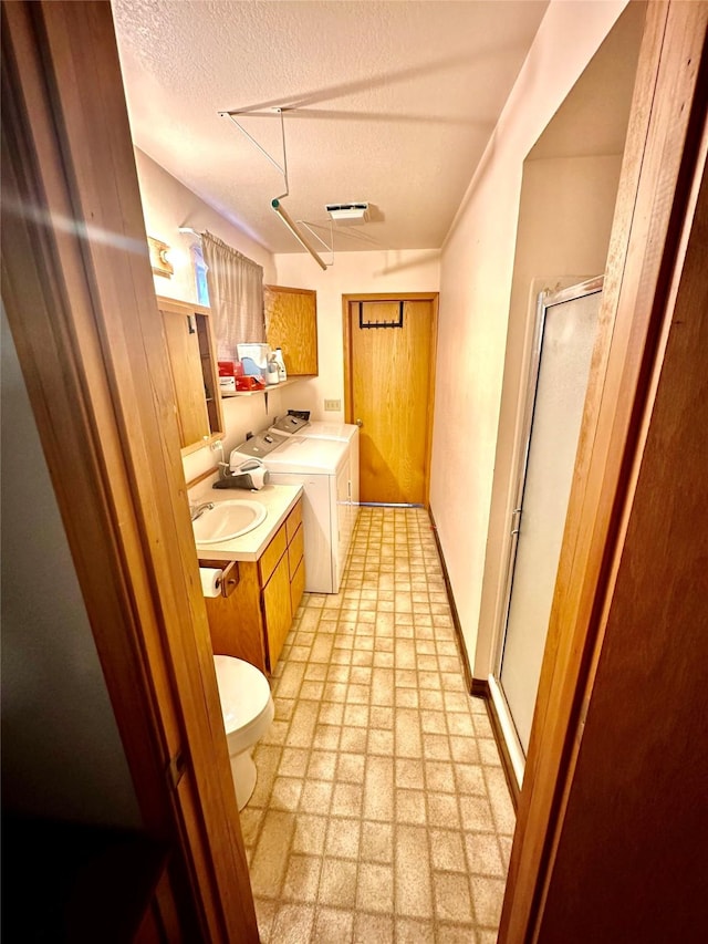 interior space with vanity, separate washer and dryer, a shower stall, a textured ceiling, and toilet