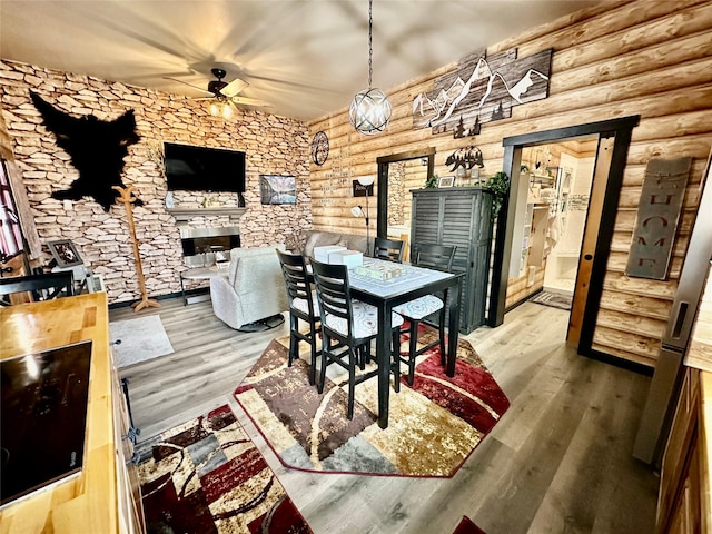 dining area featuring a ceiling fan, wood finished floors, and log walls