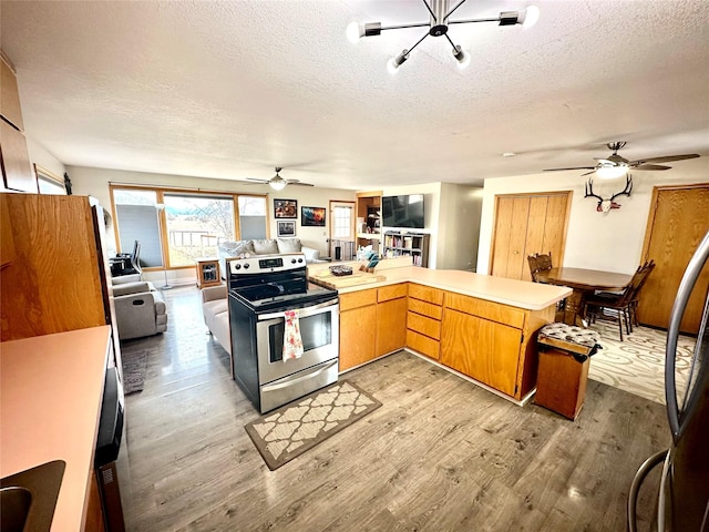 kitchen with a textured ceiling, stainless steel electric stove, open floor plan, light wood-style floors, and light countertops