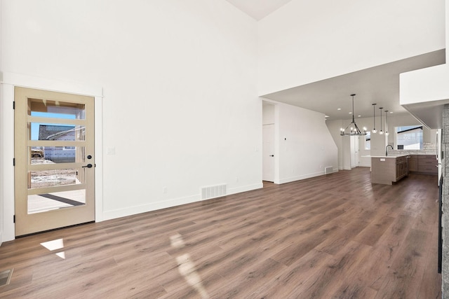 unfurnished living room featuring visible vents, baseboards, a chandelier, a towering ceiling, and wood finished floors