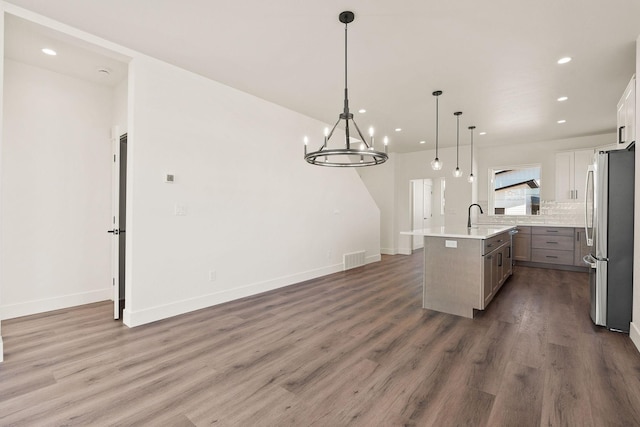 kitchen featuring wood finished floors, an island with sink, recessed lighting, freestanding refrigerator, and backsplash