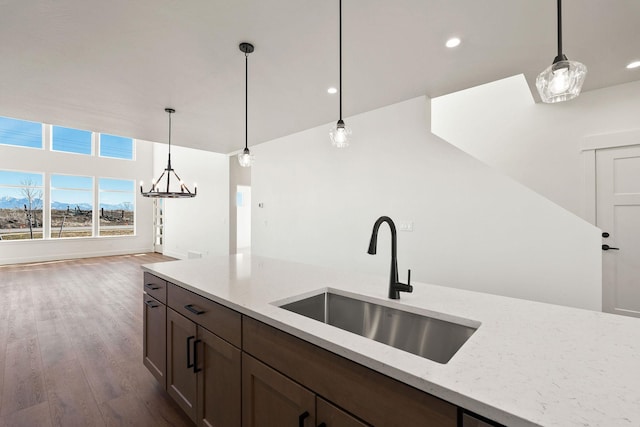 kitchen featuring a sink, light stone counters, pendant lighting, and dark wood-style floors