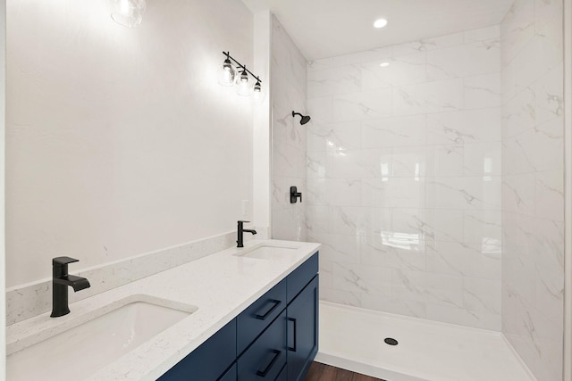 full bath featuring double vanity, recessed lighting, tiled shower, and a sink