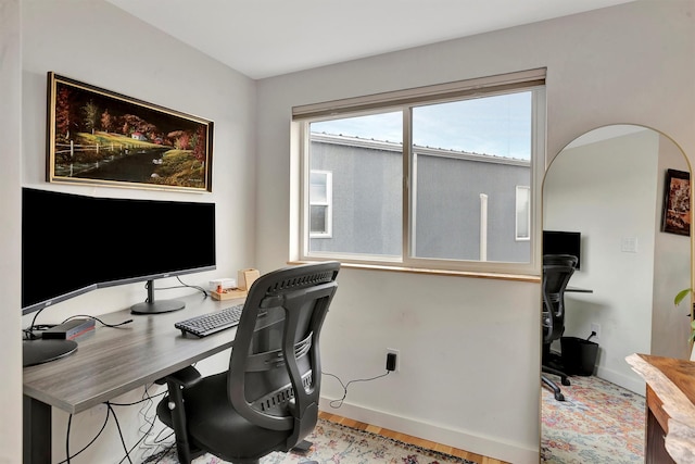 home office featuring baseboards, arched walkways, and wood finished floors