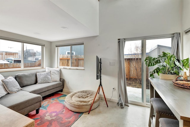 living area featuring a wealth of natural light, baseboards, and concrete floors