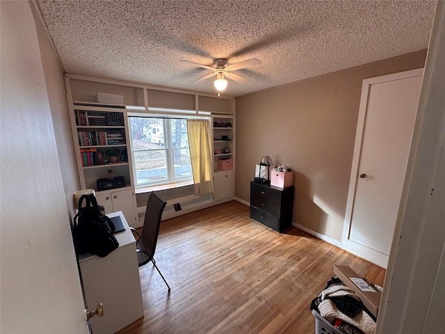 unfurnished office featuring baseboards, light wood-style flooring, a textured ceiling, and ceiling fan