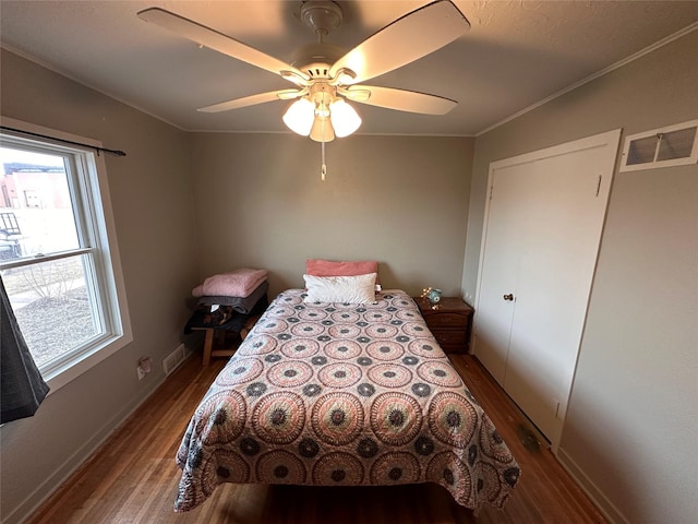 bedroom with visible vents, baseboards, ornamental molding, wood finished floors, and a ceiling fan