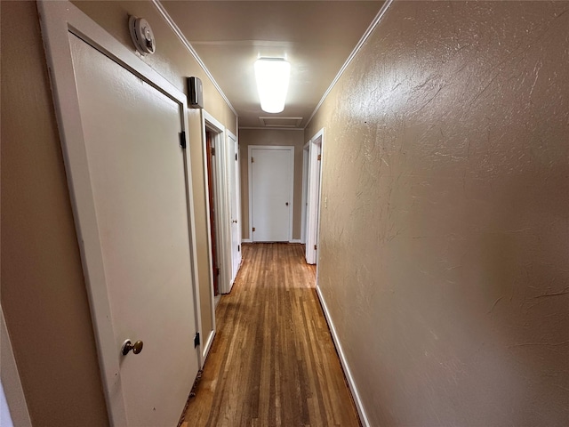 corridor featuring ornamental molding, wood finished floors, and a textured wall