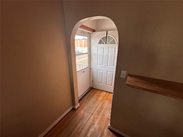 doorway featuring baseboards, arched walkways, and light wood-style floors