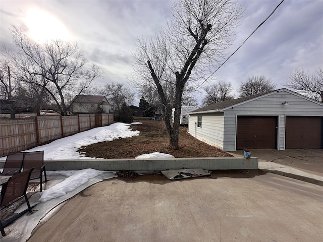 yard layered in snow featuring a detached garage, an outdoor structure, and fence