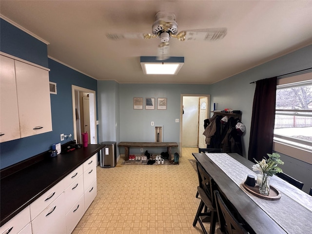 interior space with ornamental molding, dark countertops, white cabinetry, light floors, and ceiling fan