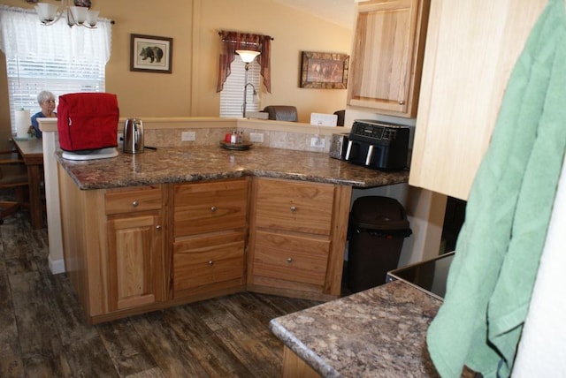 kitchen featuring a peninsula, dark wood-style flooring, and dark stone counters