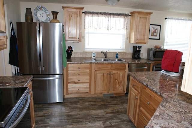 kitchen with dark stone countertops, light brown cabinets, dark wood finished floors, a sink, and appliances with stainless steel finishes