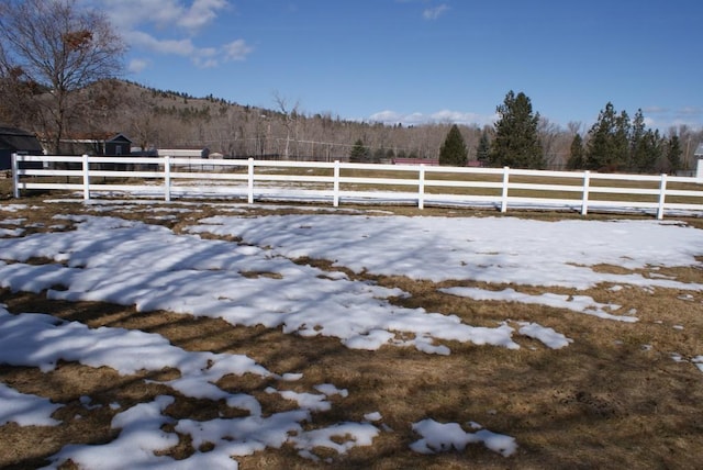 snowy yard featuring a view of trees, a rural view, and fence