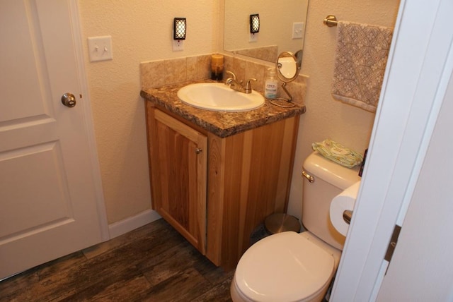 half bathroom featuring vanity, toilet, wood finished floors, and a textured wall