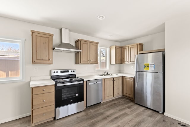 kitchen with light countertops, light wood-style flooring, wall chimney exhaust hood, and appliances with stainless steel finishes