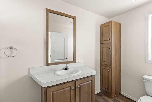 bathroom with toilet, vanity, baseboards, and wood finished floors