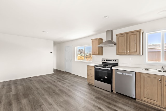 kitchen with light countertops, appliances with stainless steel finishes, dark wood-style floors, wall chimney exhaust hood, and a sink