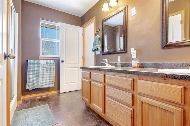 bathroom featuring double vanity, stone finish floor, a shower with door, and a sink