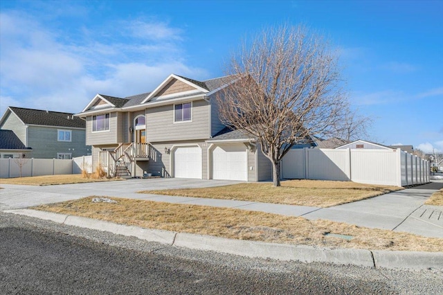 raised ranch with concrete driveway, an attached garage, and fence