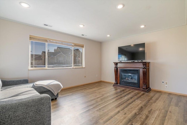 interior space featuring visible vents, baseboards, recessed lighting, wood finished floors, and a glass covered fireplace