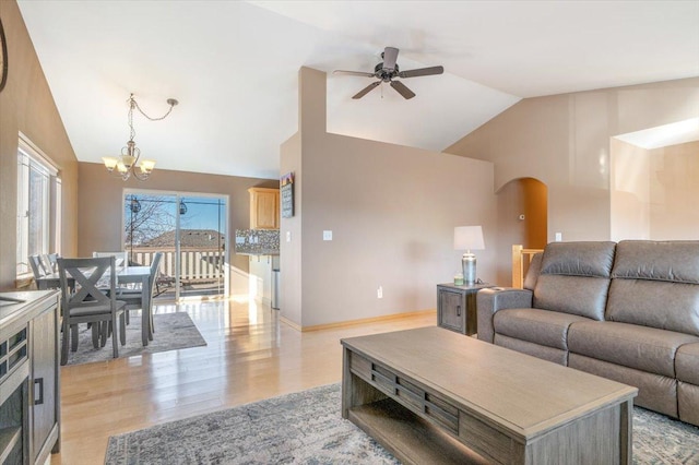 living area with light wood-style flooring, ceiling fan with notable chandelier, arched walkways, baseboards, and vaulted ceiling