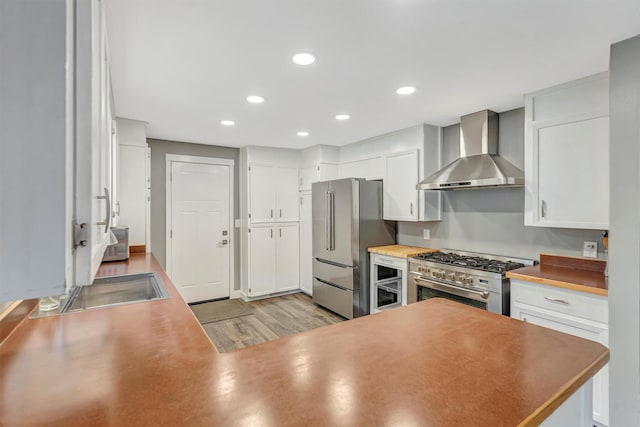 kitchen with light wood-type flooring, recessed lighting, white cabinets, wall chimney range hood, and high end appliances