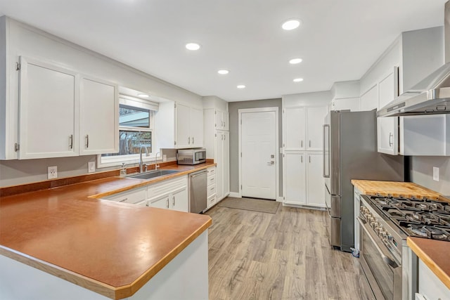 kitchen featuring a sink, white cabinetry, light wood-style floors, appliances with stainless steel finishes, and wall chimney range hood