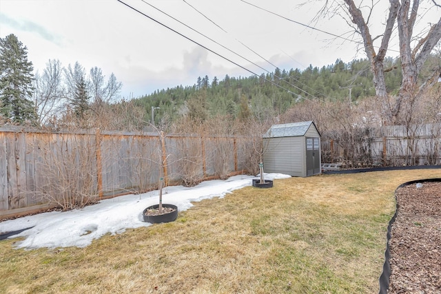 view of yard featuring a fenced backyard, an outbuilding, a storage shed, and a wooded view