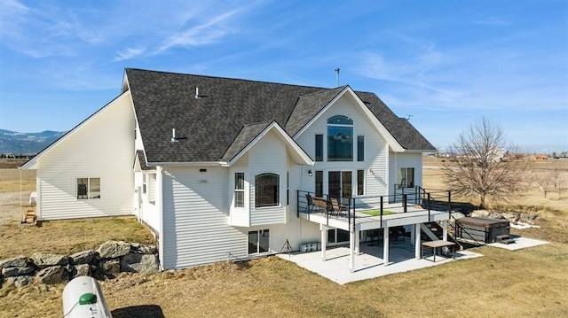 rear view of house featuring a patio, a yard, roof with shingles, and a wooden deck