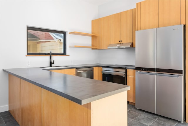 kitchen with a peninsula, a sink, under cabinet range hood, appliances with stainless steel finishes, and dark countertops