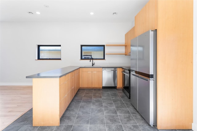 kitchen featuring light brown cabinetry, a sink, open shelves, stainless steel appliances, and a peninsula