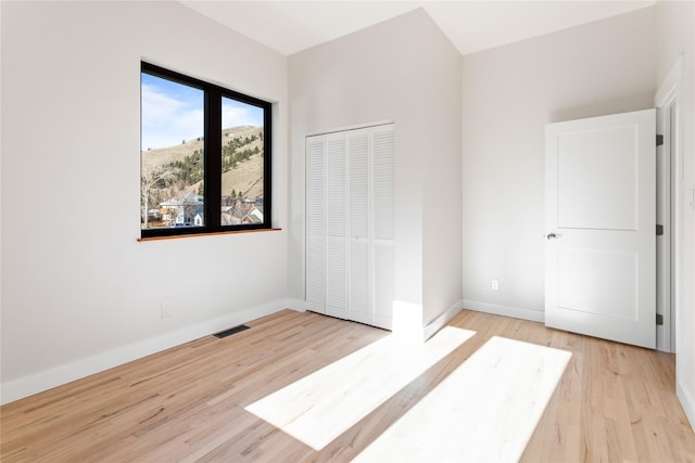 unfurnished bedroom with visible vents, wood finished floors, baseboards, and a closet