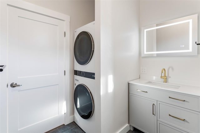 clothes washing area featuring cabinet space, stacked washing maching and dryer, dark tile patterned flooring, and a sink