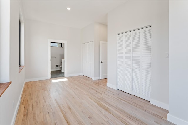 unfurnished bedroom featuring baseboards, ensuite bath, recessed lighting, light wood-style floors, and multiple closets