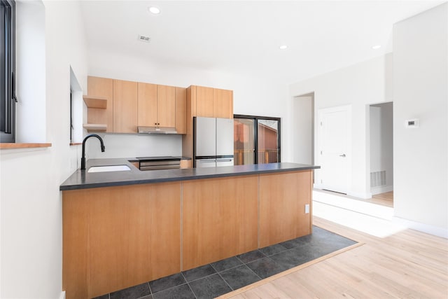 kitchen featuring a peninsula, open shelves, freestanding refrigerator, a sink, and dark countertops