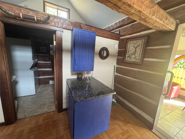 kitchen with blue cabinetry, wooden walls, and vaulted ceiling