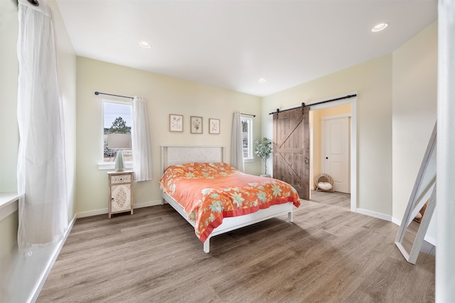 bedroom with recessed lighting, a barn door, baseboards, and light wood-style flooring