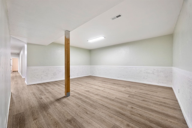 finished below grade area featuring wainscoting, brick wall, and wood finished floors