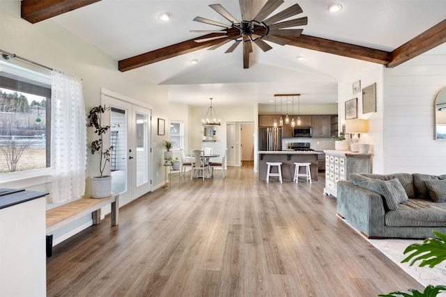 living area featuring light wood-style flooring, ceiling fan with notable chandelier, lofted ceiling with beams, french doors, and baseboards