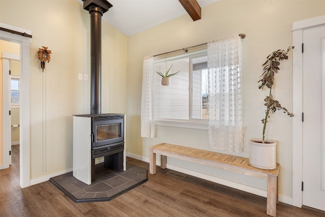 room details with beamed ceiling, visible vents, wood finished floors, baseboards, and a wood stove