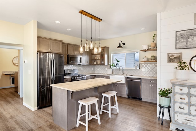 kitchen with a breakfast bar, open shelves, a sink, appliances with stainless steel finishes, and decorative backsplash