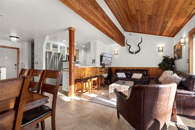 living room featuring wooden walls, a wainscoted wall, wood ceiling, light tile patterned floors, and ornate columns