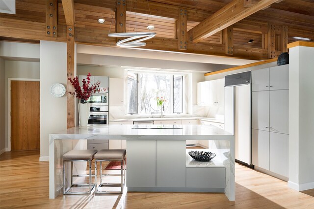 kitchen featuring paneled fridge, light wood-type flooring, oven, beam ceiling, and white cabinets