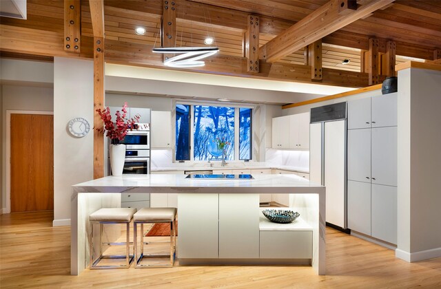 kitchen featuring paneled fridge, light wood finished floors, a breakfast bar, light countertops, and white cabinetry